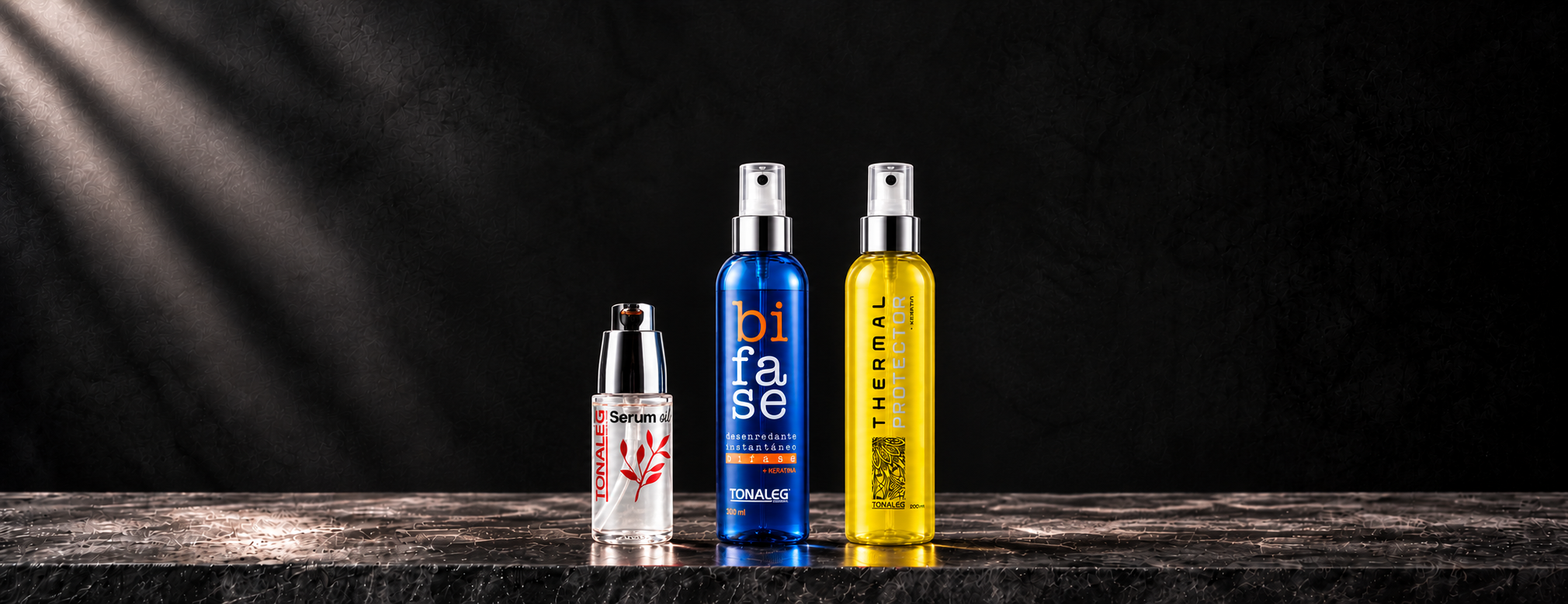 Sérum oil Tonaleg junto al bifase azul y el protector térmico amarillo del mismo tamaño, con sus reflejos sobre piedra oscura